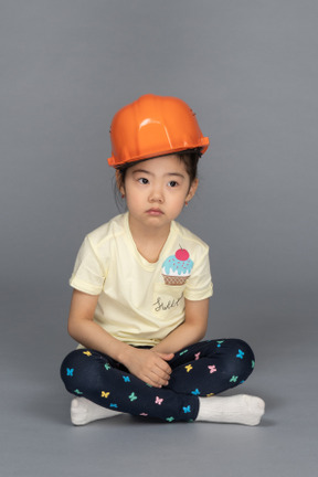 Ritratto a figura intera di una bambina che sembra pensierosa mentre indossa un cappello duro