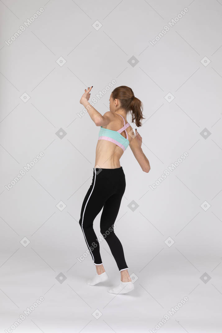 Vista traseira a três quartos de uma adolescente em roupas esportivas, andando cautelosamente na ponta dos pés