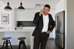 A man standing in a kitchen talking on a cell phone