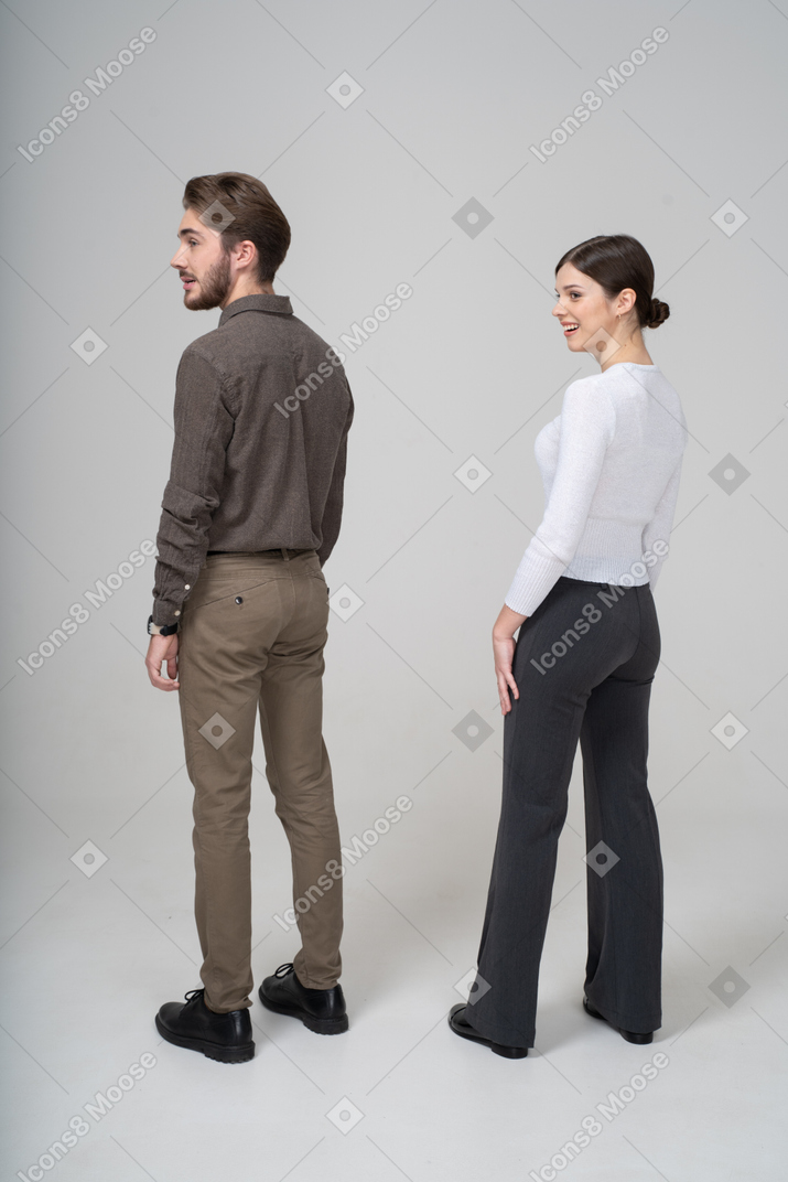 Vue arrière de trois quarts d'un jeune couple souriant confus en vêtements de bureau