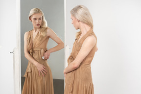 Young blond-haired person in a white towel on their hips putting on different items of clothing in front of the mirror