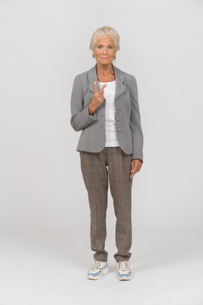 Vista frontal de uma senhora idosa de terno mostrando o sinal v
