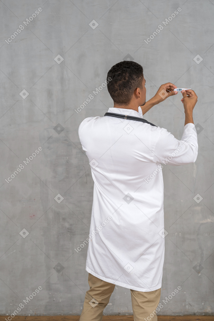 Vista traseira de um médico segurando um termômetro