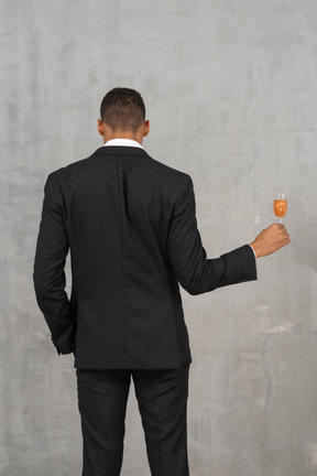 Young man standing with his back toward the camera and holding a flute glass