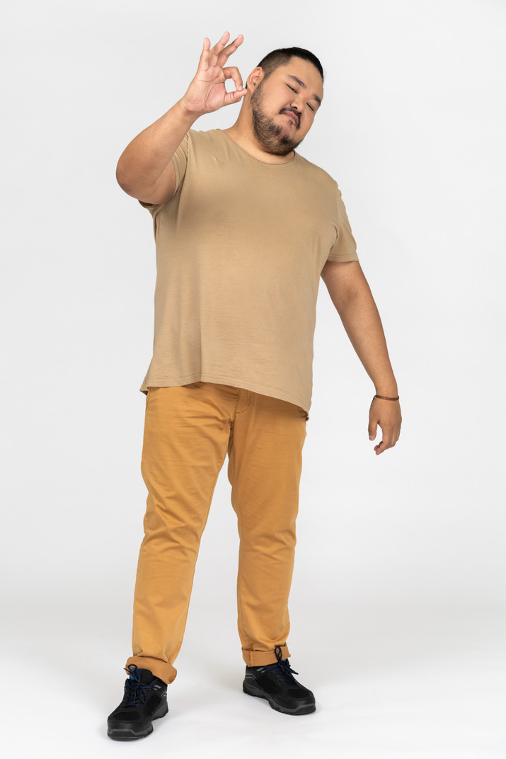 Plump asian man keeping his eyes closed and making ok gesture