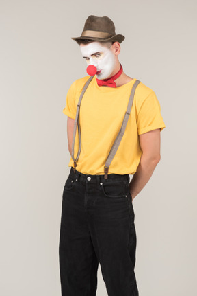 Sad male clown standing with hands behind the back