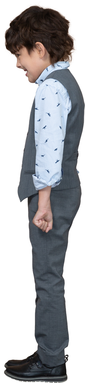 Vista lateral de un niño enojado en traje gris de pie con los puños cerrados