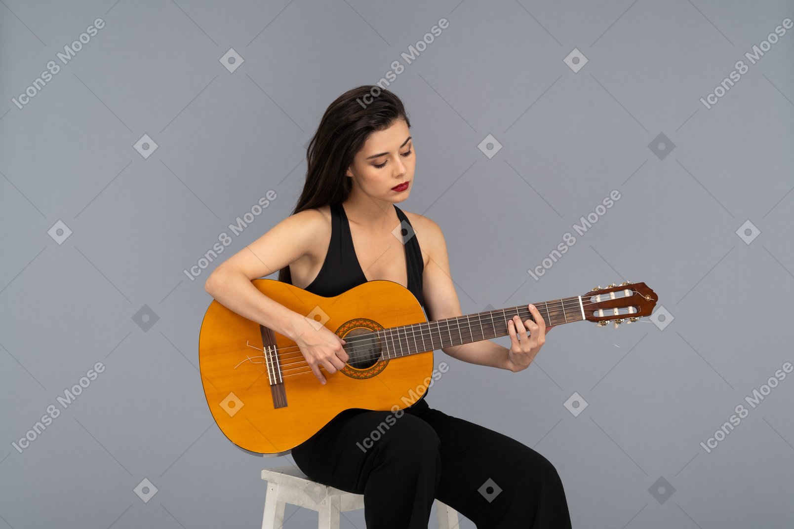 Vista frontal de una joven sentada en traje negro tocando la guitarra