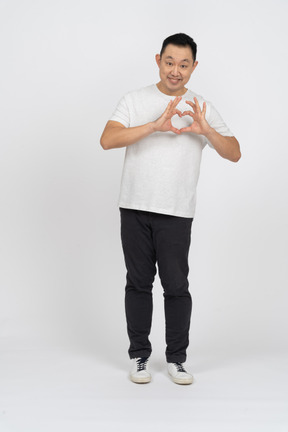 Вид спереди счастливого человека в повседневной одежде, делающего сердце пальцами и смотрящего в камеру