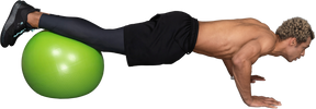 Vista lateral de un hombre afro sin camisa haciendo flexiones en una pelota de gimnasia