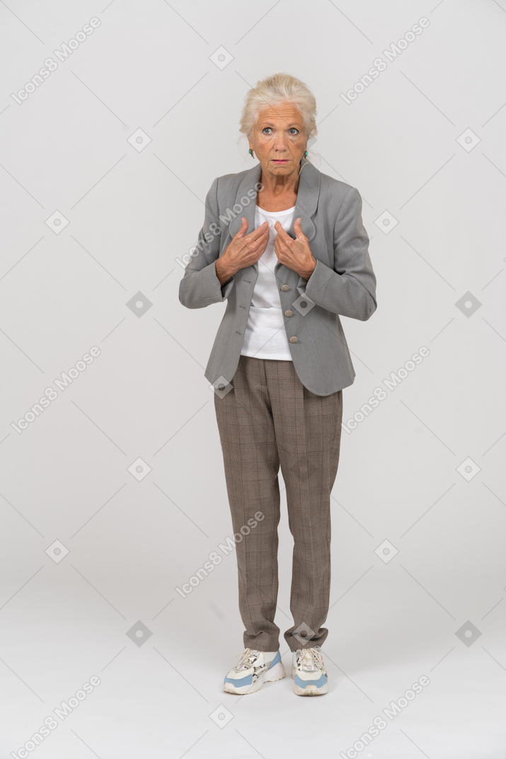 Vista frontal de una anciana impresionada en traje apuntando a sí misma