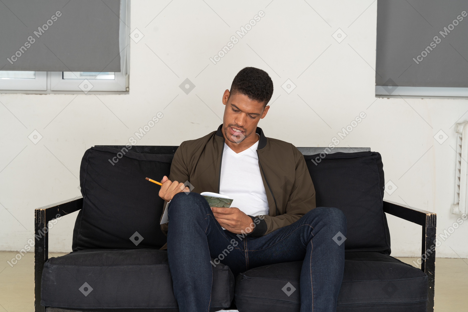 Vorderansicht eines jungen mannes, der auf einem sofa sitzt und sich notizen macht