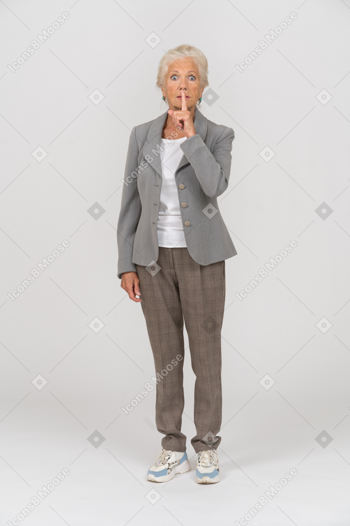 Vista frontal de uma senhora idosa de terno fazendo um gesto de shh