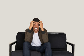 Mad looking young man sitting on the sofa and touching his head with hands