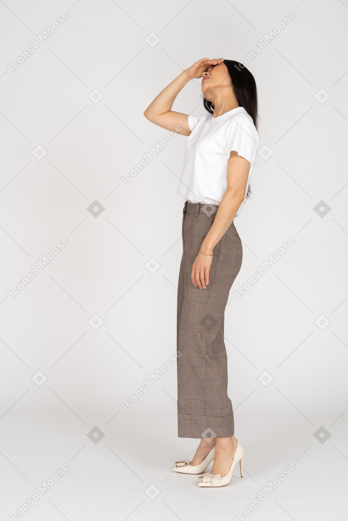 一位年轻的女士在马裤和t恤举起的侧视图听到手时抬头