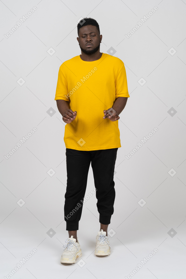 彼の腕のダウを伸ばしている黄色のtシャツを着た若い浅黒い肌の男の正面図