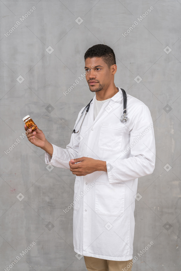 Doctor con estetoscopio sosteniendo un frasco de pastillas