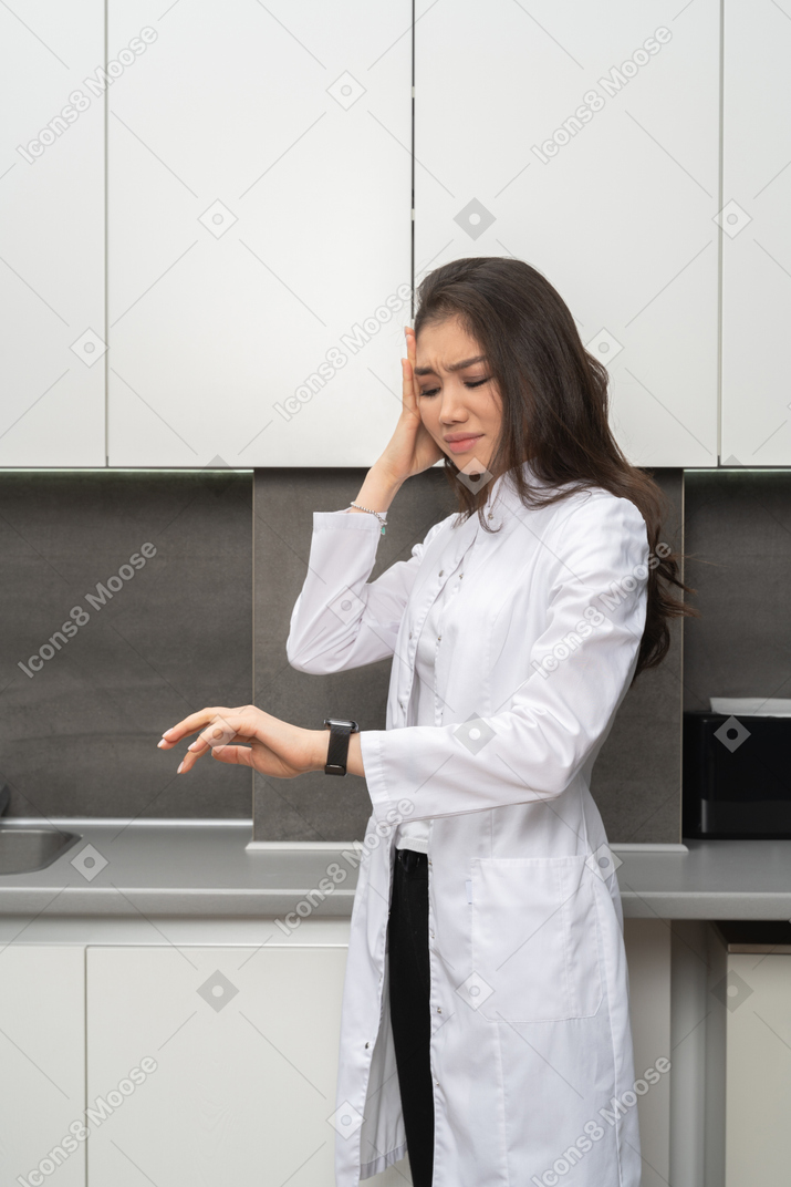 Расстроенная женщина в белом халате проверяет время