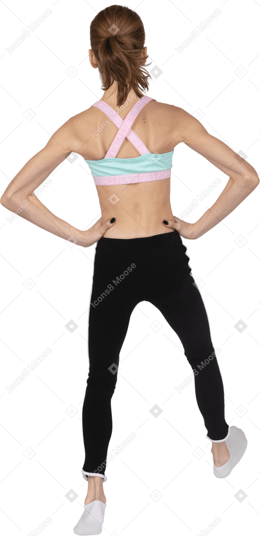 Vista posterior de una jovencita en ropa deportiva poniendo las manos oh caderas y doblando las rodillas