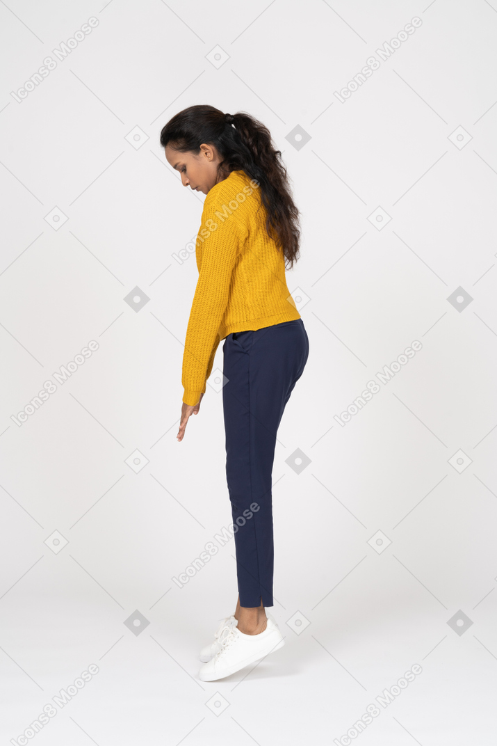 Vista laterale di una ragazza in abiti casual in piedi sulle punte dei piedi e guardando in basso