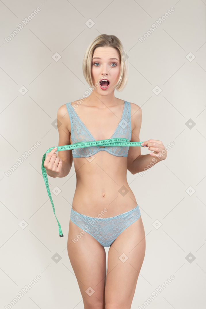 Surprised young woman in lingerie meausring her chest