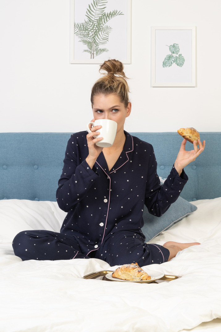 Front view of a young lady in pajamas having breakfast in bed