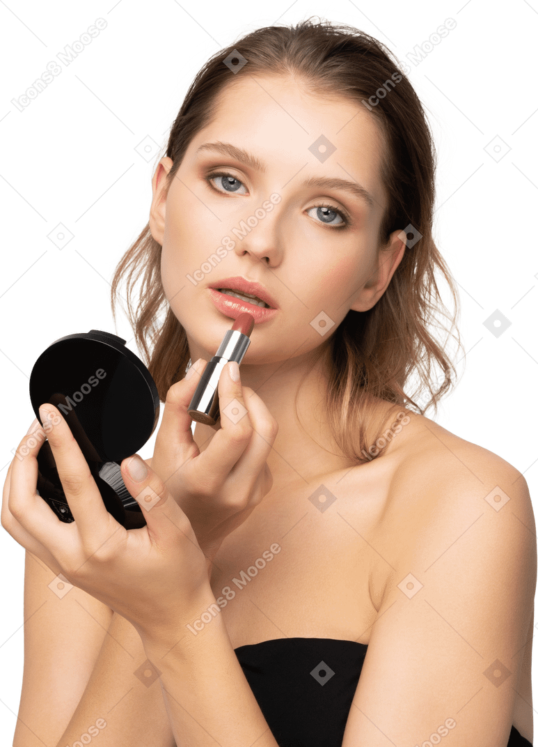 Front view of a young woman applying lipstick while holding a mirror