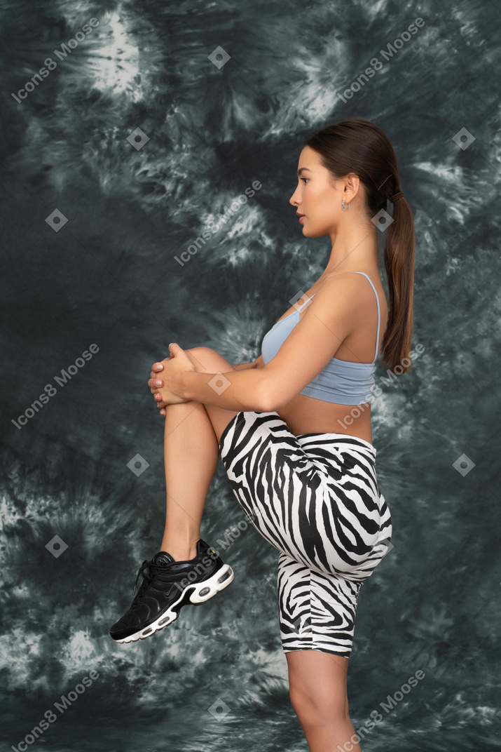 Retrato lateral de la atleta femenina presionando su rodilla contra el pecho