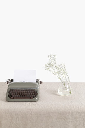Glass vase with twig and vintage typewriter on the table