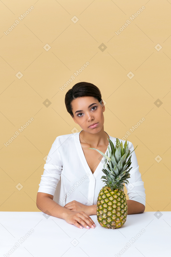 Girl in white dress sitting at the table with pineapple on it