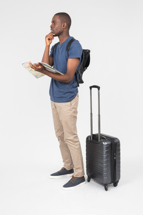 Pensive male tourist holding map and standing near luggage