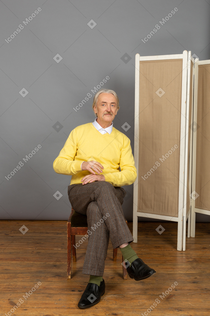 Uomo sorridente seduto su una sedia e guardando da parte