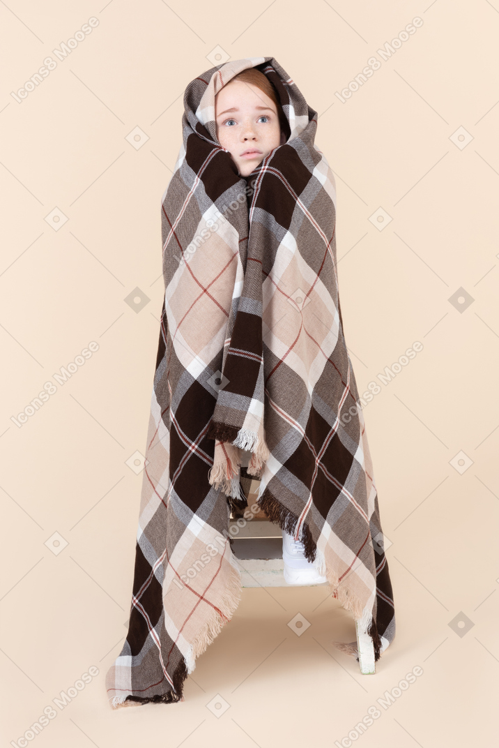 Teenage girl sitting wrapped in checked blanket