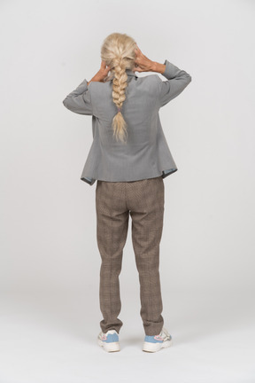 Vista posterior de una anciana en traje cubriendo las orejas con las manos