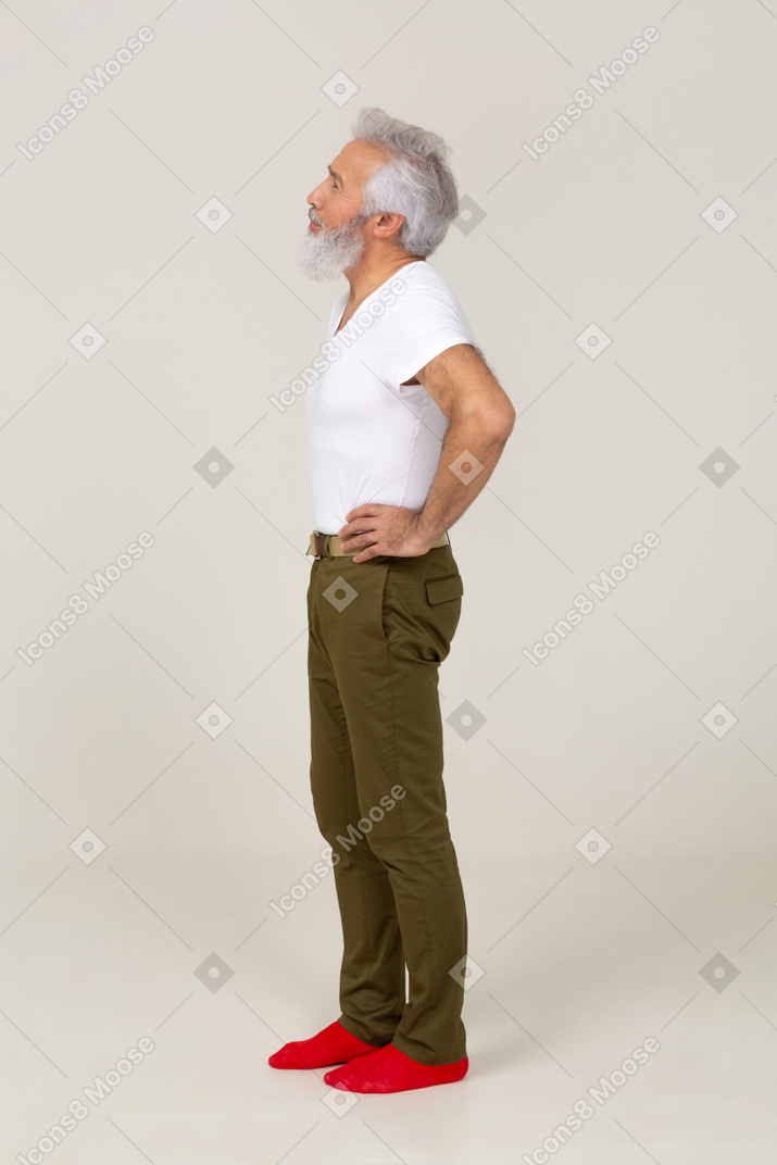 Vista lateral de um homem distraído em pé com as mãos na cintura