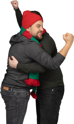 拳を握りしめている2人の感情的に抱き締める男性のサッカーファンの側面図