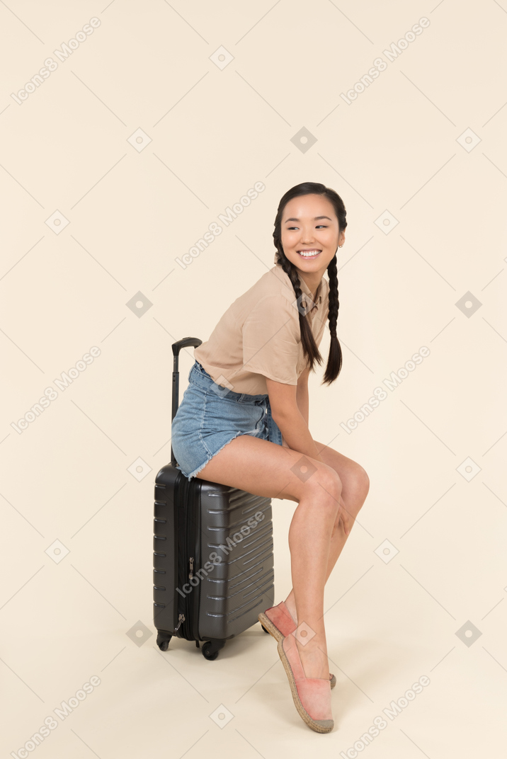 가방에 앉아 웃는 젊은 여성 여행자