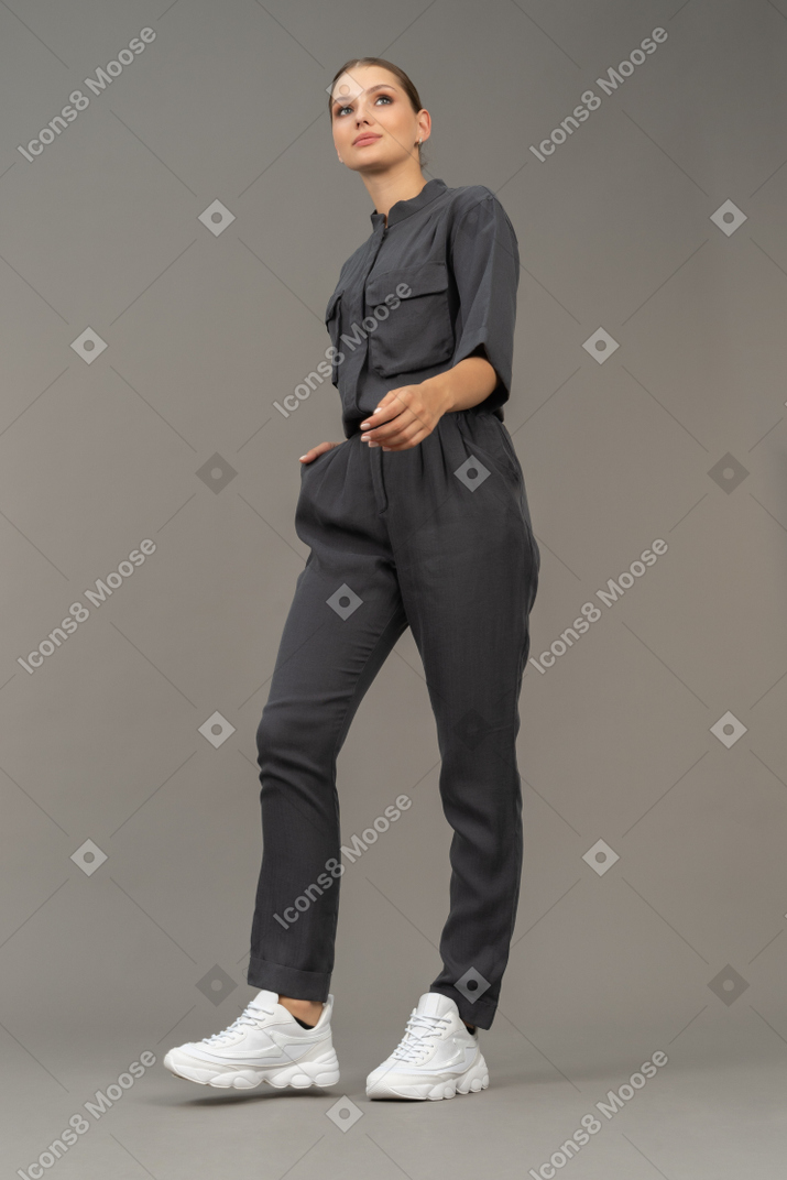 Three-quarter view of a walking young woman in a jumpsuit holding hand in pocket