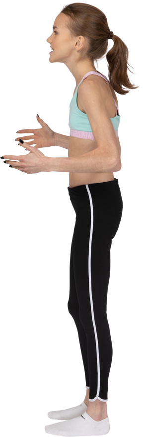 Vista lateral de uma adolescente em roupas esportivas levantando as mãos e olhando para o lado