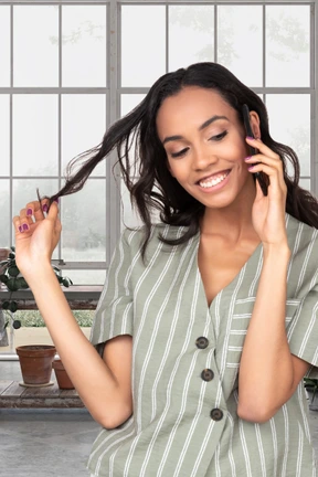 A woman rolling a strand of hair while talking on a phone