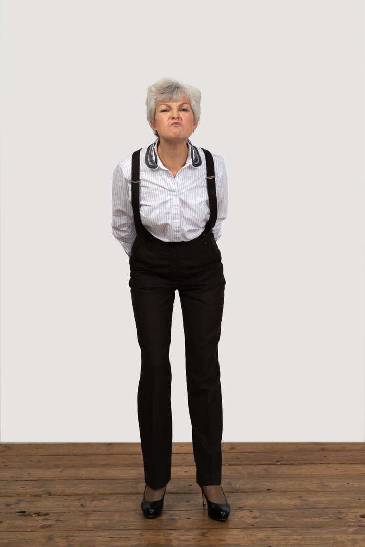 Front view of an old  naughty female in office clothes bending down and grimacing