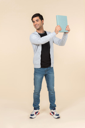 Young caucasian man pointing at book he's holding