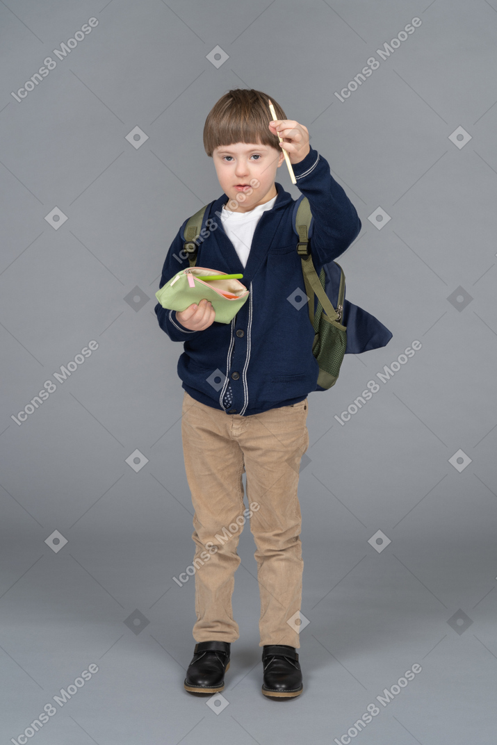Portrait of a little boy with a backpack holding up a pencil