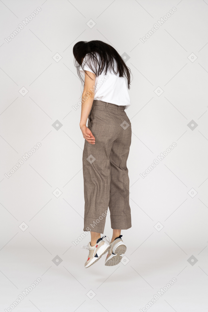 Vista posteriore di tre quarti di una giovane donna che salta in calzoni e t-shirt guardando verso il basso