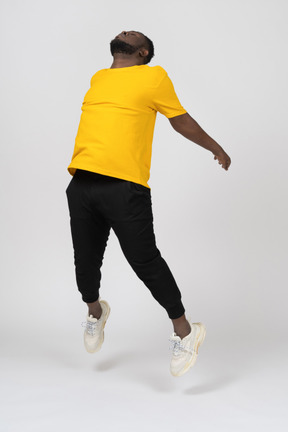 Three-quarter view of a jumping young dark-skinned man in yellow t-shirt outspreading hands