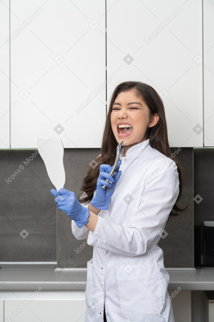 Vista de tres cuartos de una dentista asustada sosteniendo un espejo e instrumento dental