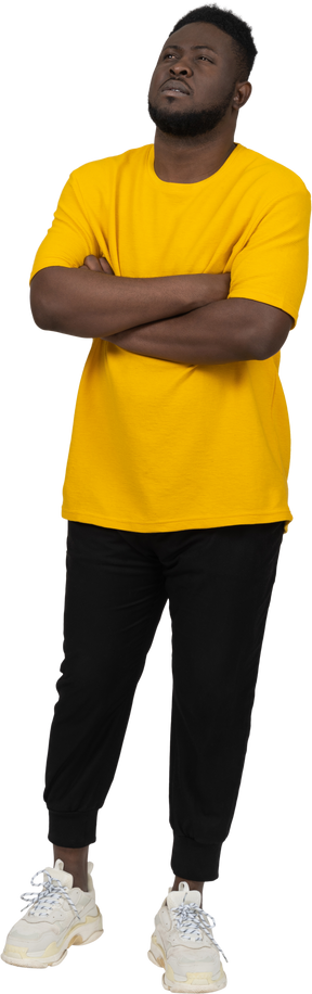 Vista di tre quarti di un giovane uomo sospettoso dalla pelle scura con una maglietta gialla che incrocia le braccia
