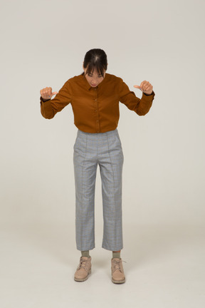 Vista frontal de una joven mujer asiática en calzones y blusa mostrando los pulgares hacia abajo