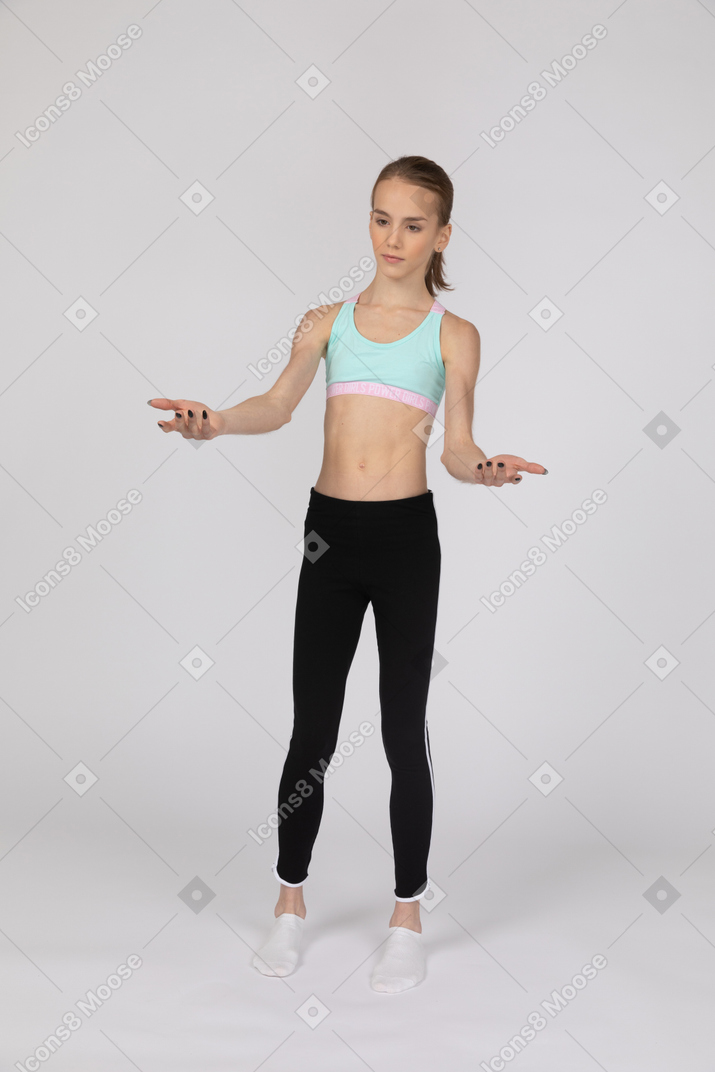 Una adolescente en ropa deportiva de pie con las manos levantadas.