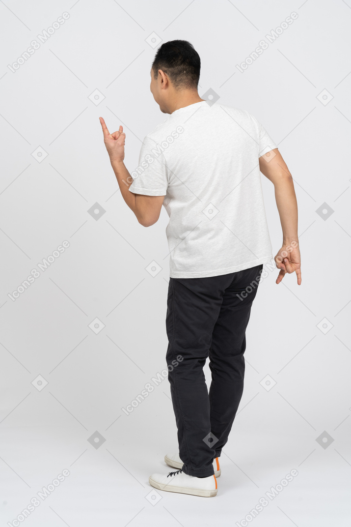 Мужчина в повседневной одежде стоит спиной к камере и показывает рок-жест